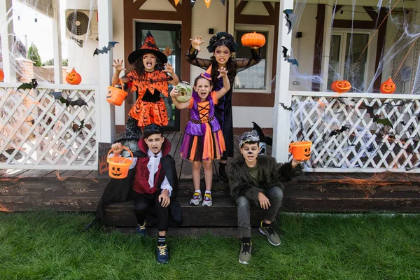 Crianças Multiétnicas Trajes Halloween Sorrindo Mostrando Gestos Assustadores Perto Casa — Fotografia de Stock