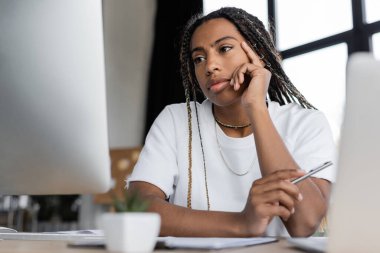 Ofiste bilgisayarların yanında elinde kalem tutan Afrikalı Amerikalı iş kadını. 
