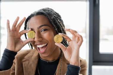 KYIV, UKRAINE - 27 Nisan 2022: Ofiste bitcoin tutan neşeli Afro-Amerikan iş kadını 