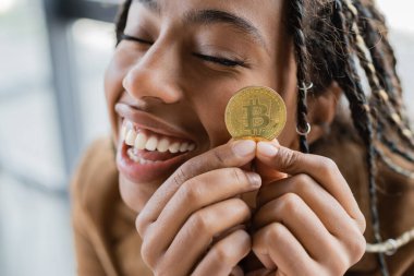 KYIV, UKRAINE - 27 Nisan 2022: Pozitif Afro-Amerikan iş kadını ofisinde altın bitcoin tutuyor 