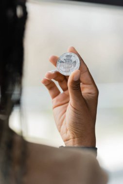 KYIV, UKRAINE - 27 Nisan 2022: Bulanık Afrikalı Amerikalı iş kadını ofisinde gümüş bitcoin tutuyor 
