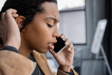 Ciddi Afro-Amerikan iş kadınlarının ofisteki akıllı telefonlardan konuşmalarının yan görüntüsü. 