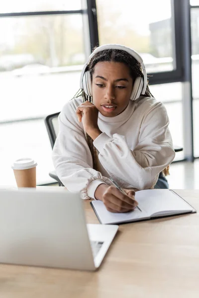 Mujer Negocios Afroamericana Auriculares Escribiendo Cuaderno Mirando Computadora Portátil Oficina — Foto de Stock