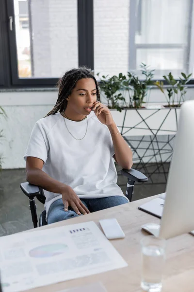 African american businesswoman in casual clothes looking at computer near smartphone in office