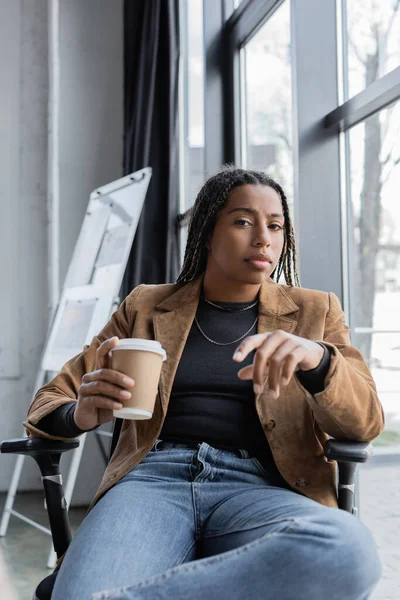 African american businesswoman in jeans and jacket holding coffee to go in office