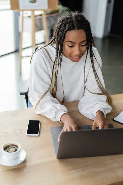Mosolygós Afro Amerikai Üzletasszony Használja Laptop Közelében Kávé Okostelefon Irodában — Stock Fotó