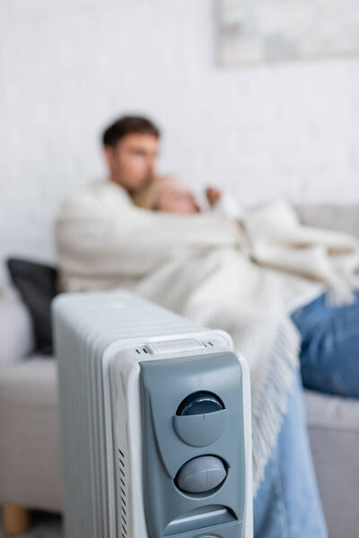 modern radiator heater near blurred couple under blanket in living room 