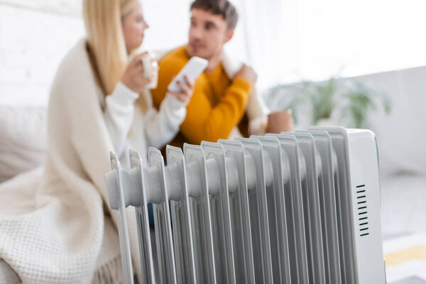 modern radiator heater near blurred couple covered with blanket 