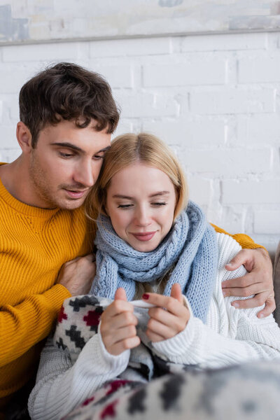 caring man hugging sick blonde woman with digital thermometer 