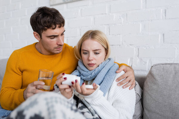 caring man holding glass with water and hugging sick girlfriend with medicaments  