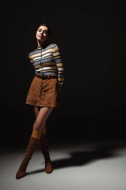 Çizgili balıkçı yakalı, etekli ve çizmeli siyah elbiseli bir kadın. 