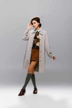 Trençkotlu zarif genç bir kadın. Gri bereyi düzeltiyor.