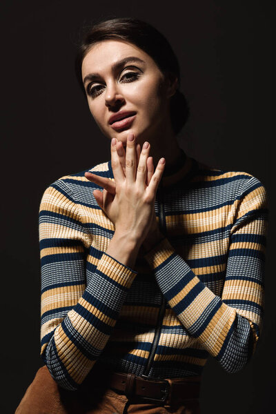 young woman in striped turtleneck looking at camera isolated on black 