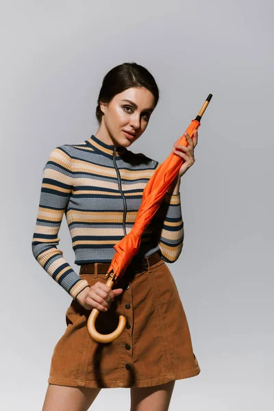 young woman in long sleeved turtleneck and skirt posing with bright umbrella isolated on grey