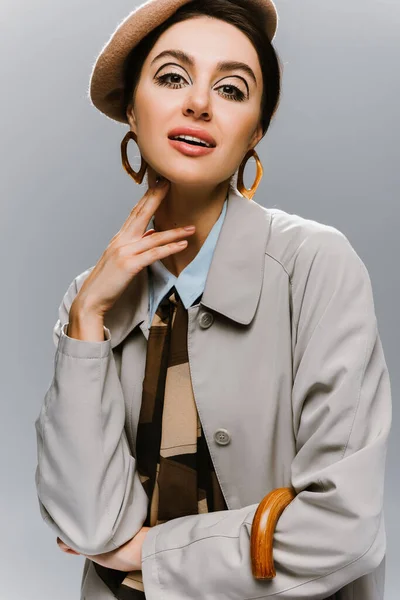 portrait of pin up young woman in beret and trench coat posing isolated on grey