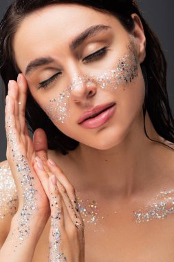 portrait of sleepy young woman with sparkling glitter on cheeks and hands isolated on grey  clipart