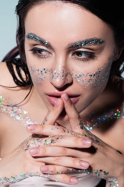 portrait of pensive woman with glitter on face and body looking away isolated on grey