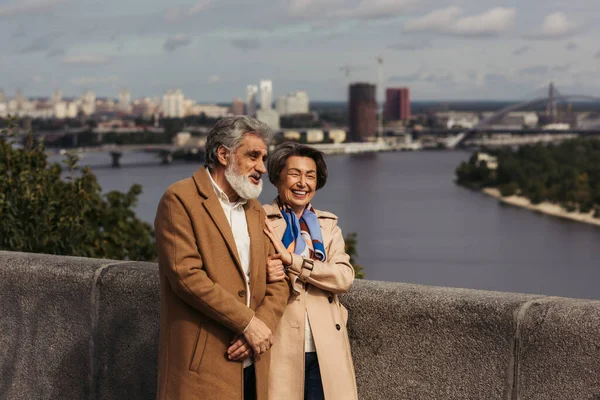 Feliz Pareja Ancianos Abrigos Beige Sonriendo Caminando Puente Cerca Del — Foto de Stock