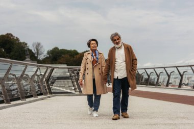 Paltolu mutlu yaşlı çift el ele tutuşup, köprüde yürüyorlar. 