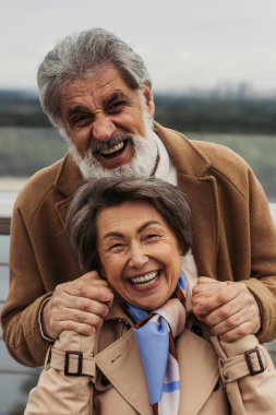 Mutlu yaşlı adam ve bej ceketli neşeli kadının portresi gülümsüyor ve kameraya bakıyor. 