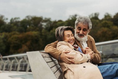 Mutlu kıdemli adam dışarıda bankta otururken neşeli karısına sarılıyor. 