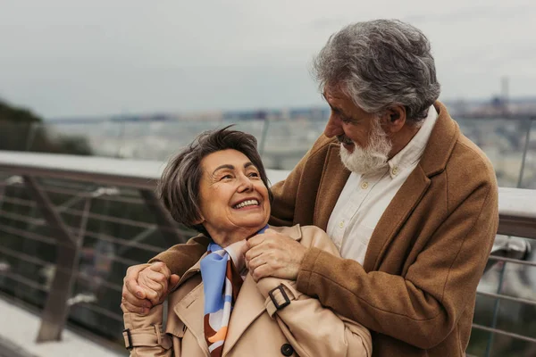 Ευτυχισμένος Ηλικιωμένος Άντρας Αγκαλιάζει Θετική Σύζυγο Μπεζ Παλτό Και Χαμογελά — Φωτογραφία Αρχείου