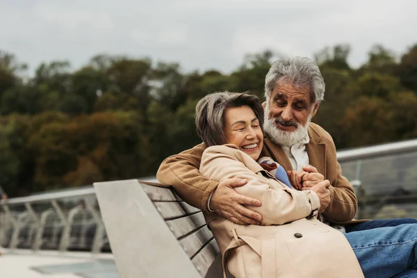 Happy Senior Man Hugging Joyful Wife While Sitting Bench Outdoors — Stock Photo, Image