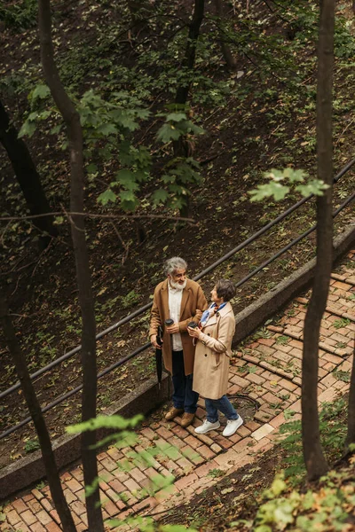 穿着米黄色外套 手持纸杯 在公园里散步的快乐的退休夫妇的高角镜 — 图库照片