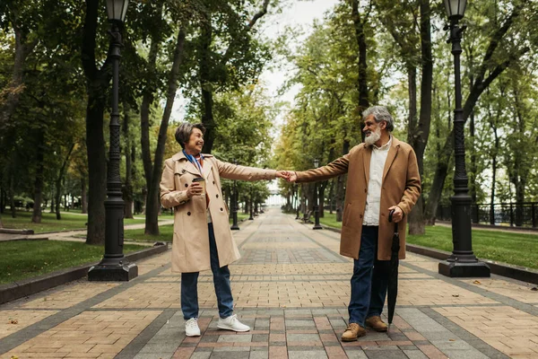 全长的老年妇女 戴着纸杯 手牵着手 有时髦的丈夫穿着外套 — 图库照片