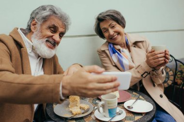 Kahvaltının ortasında neşeli karısıyla selfie çeken mutlu bir son sınıf öğrencisi. 