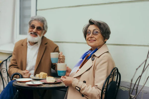 戴着眼镜的快乐的老妇人 一边举杯 一边在阳台上与长胡子的丈夫共进午餐 — 图库照片