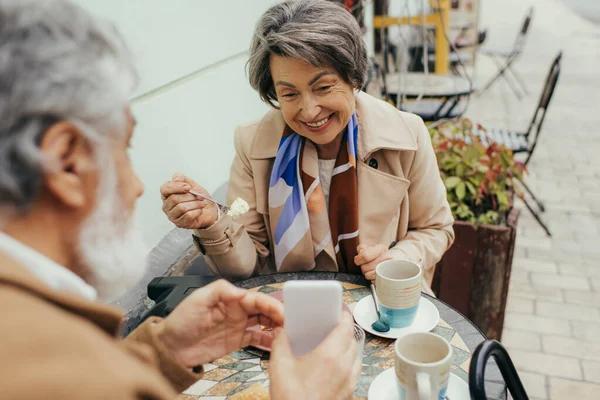 Vousatý Starší Muž Ukazuje Smartphone Šťastné Ženě Při Snídani Terase — Stock fotografie