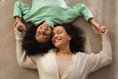 Gülümseyen Afrikalı Amerikalı kızın neşeli annesiyle birlikte halının üzerinde yatışı. 