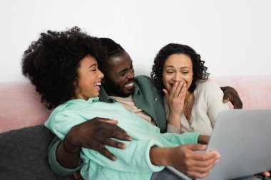 Pozitif Afro-Amerikan ailesi oturma odasında dizüstü bilgisayardan komedi filmi izliyor. 