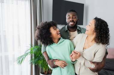 Komik afro-amerikalı adam evde neşeli genç kız ve karısına sarılıyor.