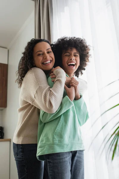 Complacida Mujer Afroamericana Sonriendo Mientras Abraza Emocionada Hija Preadolescente —  Fotos de Stock