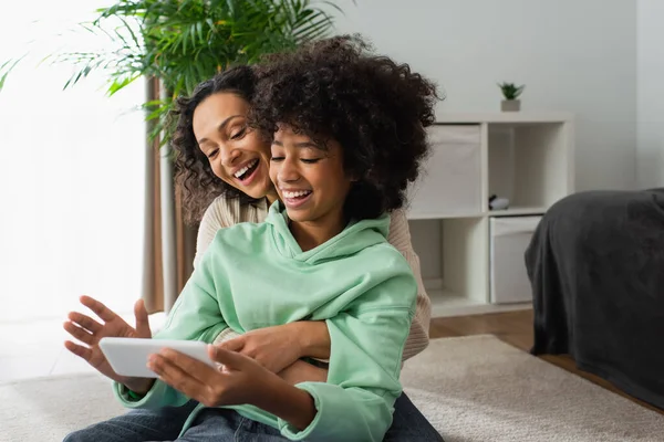 快乐的非洲裔美国少女和卷曲的母亲在客厅里用手机 — 图库照片