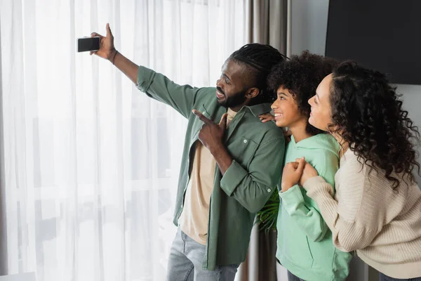 快乐的非洲裔美国人 拿着智能手机和家人一起自私自利 在家里微笑 — 图库照片