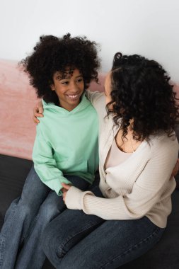 Annenin mutlu bir ergen kızla el ele tutuşup koltukta oturduğu yüksek açılı manzara.