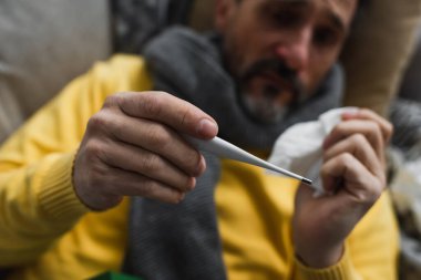 Elektronik termometrenin seçici odağı bulanık arkaplanda ateşten muzdarip hasta bir adam üzerinde.