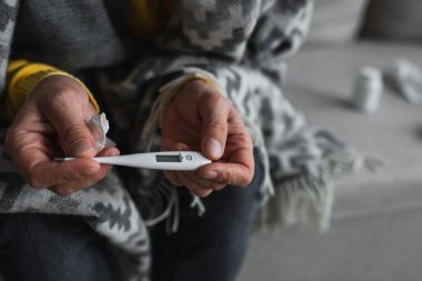 Ateşten muzdarip, elinde elektronik alet tutan hastalıklı bir adamın kısmi görüntüsü