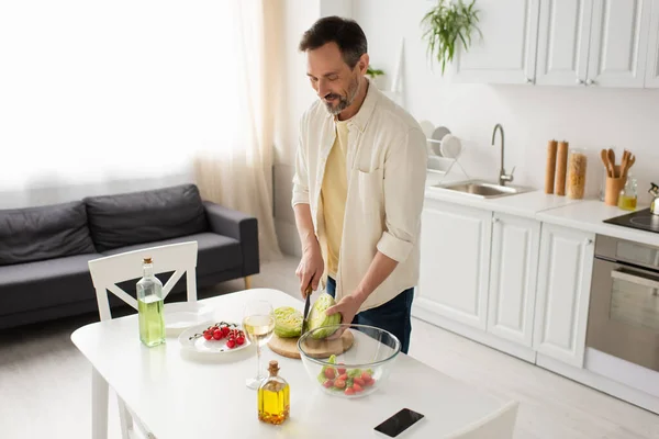 Hombre Sonriente Cortando Lechuga Cerca Del Tazón Con Ensalada Verduras — Foto de Stock