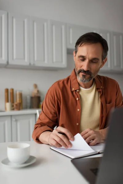 Man Met Baard Zitten Met Notebook Buurt Wazig Laptop Koffie — Stockfoto