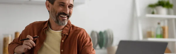 Hombre Barbudo Alegre Sosteniendo Pluma Sonriendo Cerca Borrosa Portátil Bandera —  Fotos de Stock