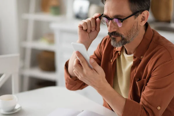 Homem Barbudo Ajustando Óculos Olhando Para Telefone Celular Fundo Embaçado — Fotografia de Stock