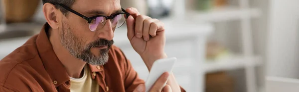 Gri Sakallı Bir Adam Gözlüklere Afişe Dokunurken Akıllı Telefona Bakıyor — Stok fotoğraf