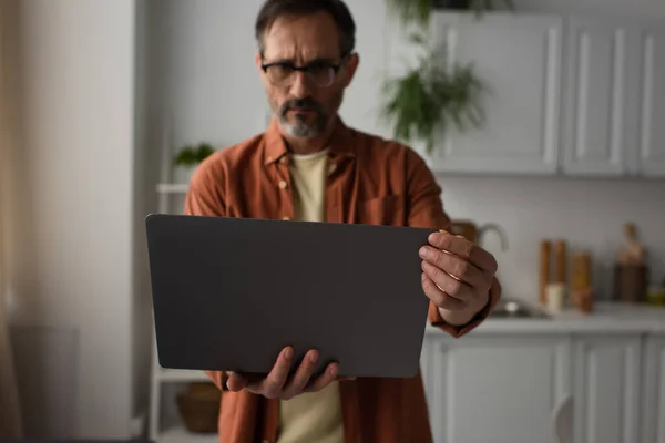 Bezorgde Man Bril Kijkt Laptop Wazige Keuken — Stockfoto