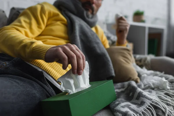 ソファに寝そべって紙ナプキンを持って行く病気の男の部分的な見解 — ストック写真