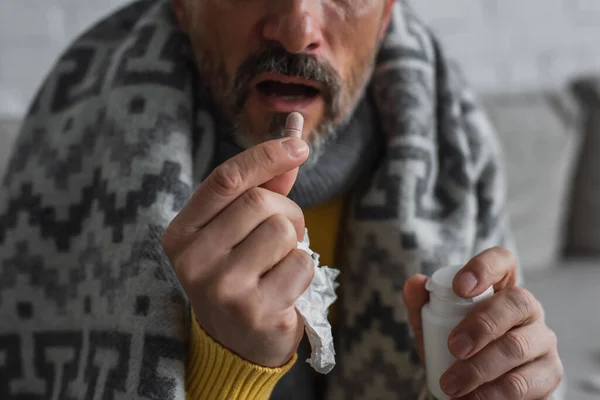 partial view of diseased man with paper napkin taking pill on blurred background