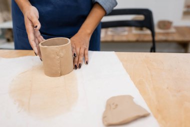 Çömlekçilik kursunda mavi önlüklü Amerikalı genç bir kadının kilden bir şeyler modellemesine kısmi bakış açısı 